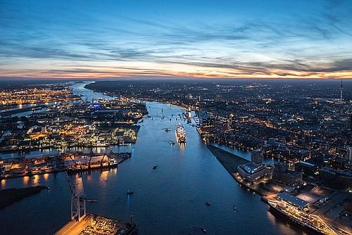 Blick von oben auf die Elbe und den Hafen von Hamburg. Die Sonne ist gerade untergegangen und alles ist beleuchtet. 